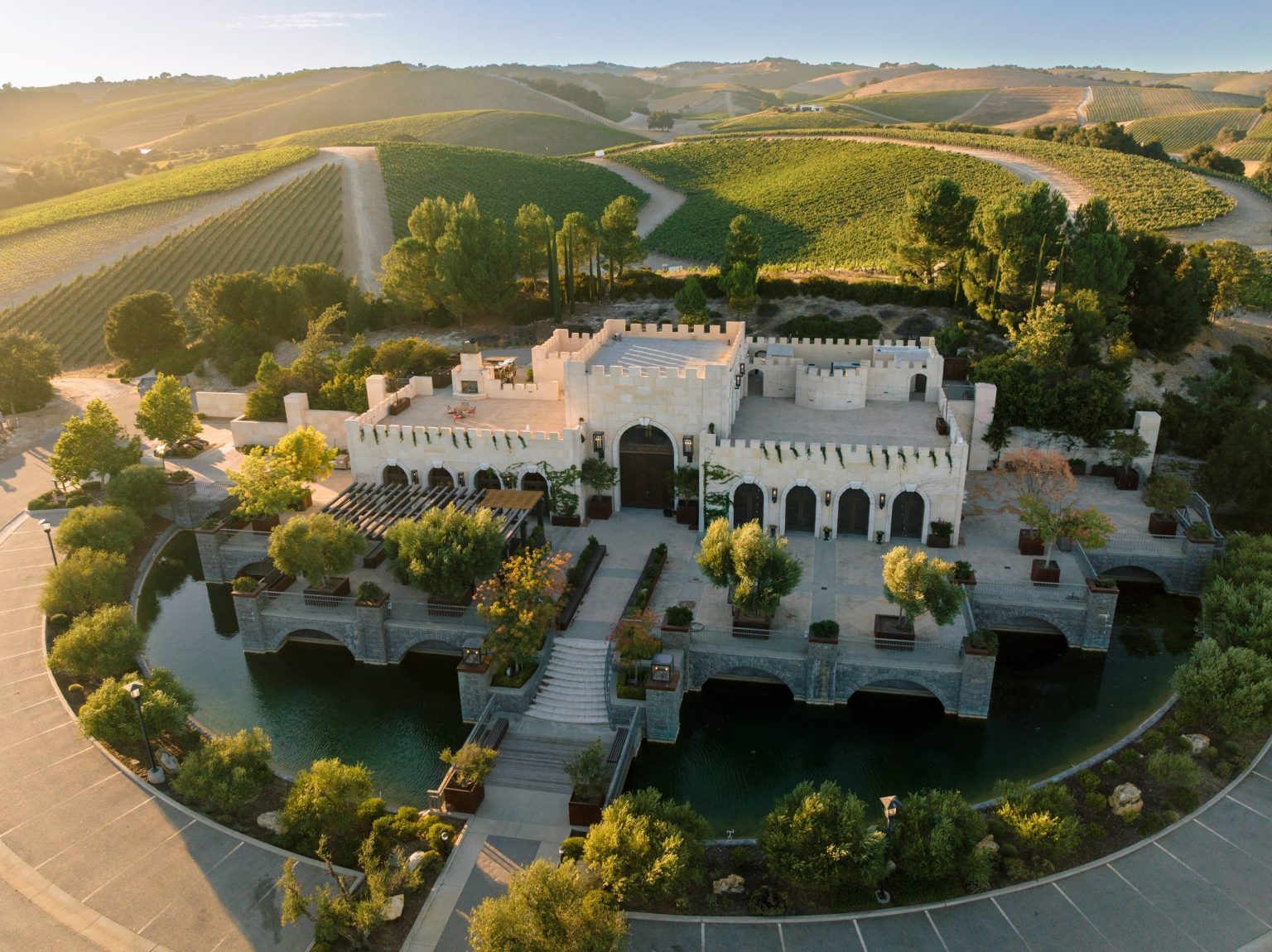Castle-style building with arched entrances and a reflecting pool, surrounded by vineyard hills in Paso Robles