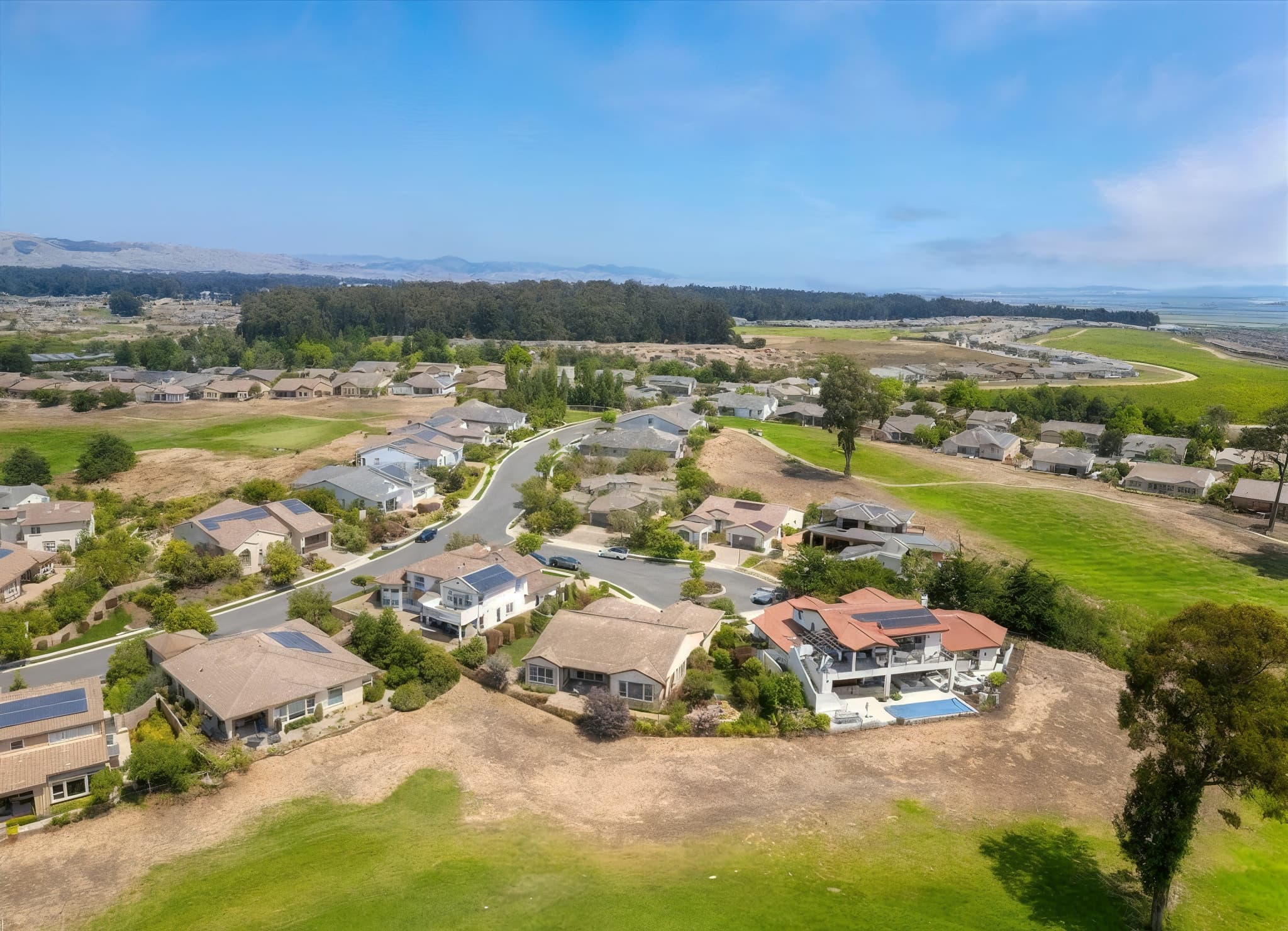 Aerial view of homes along a curving street in a Nipomo, California neighborhood, with green hills and open land beyond